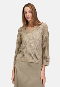 Pull en maille beige clair avec un décolleté en V ample, des manches trois-quarts et un motif aéré. Associé à une jupe beige unie.