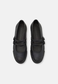 Sapatos pretos com biqueira arredondada, feitos de um material semelhante à borracha liso. Apresentam duas tiras ajustáveis na parte média do pé. Sola texturizada.