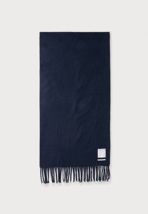 Écharpe rectangulaire bleu marine foncé avec bords frangés et une petite étiquette blanche près d’un coin sur un fond uni.