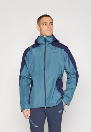 Chaqueta ligera y resistente al agua en azul con acentos en navy. Cuenta con capucha, bolsillos con cremallera y tejido texturizado en los hombros.