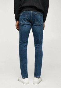 Tummansiniset, kapeat farkut, joissa takataskut ja hienovaraiset ompelut, yhdistettyinä valkoisiin lenkkareihin.