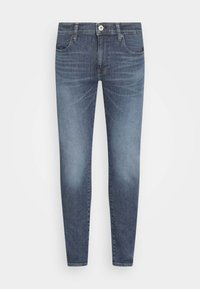 Vaqueros de denim ajustados en azul oscuro. Presenta un diseño clásico de cinco bolsillos, cierre de cremallera y un ligero desgaste en los muslos.