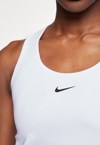 Bjela sportska majica bez rukava napravljena od rastezljivog materijala, s okruglim izrezom i malim crnim Nike logotipom na sredini.
