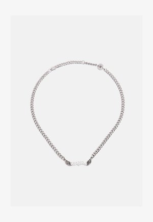 Sølvsmykke med kjede og vingformede detaljer på hver side av et sentralt tekstmotiv, lagt flatt på en hvit bakgrunn.