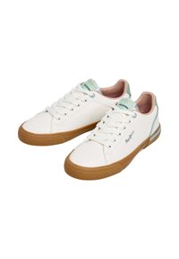 Baskets blanches en toile avec une semelle en caoutchouc légèrement texturée, accents vert clair au talon et lacets blancs. Détail de logo remarquable sur le côté.