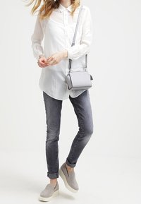 Valkoinen nappikauluspaita, harmaat farkut, harmaat liukusandaalit valkoisilla vaihteilla sekä pieni harmaa olkalaukku. Yksinkertainen, puhdas muotoilu ilman näkyviä kuvioita.