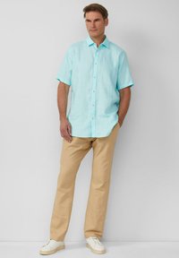 Camicia blu chiaro a maniche corte con bottoni in lino, abbinata a pantaloni beige e sneakers bianche. Texture liscia; design e palette di colori semplici.