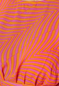 Textile multicolore présentant un motif en zigzag rose vif et orange. Le tissu a une texture lisse avec des lignes créant de la profondeur.