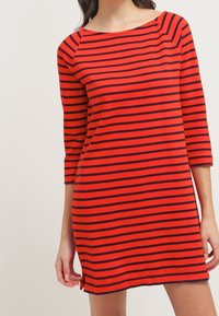 Robe rayée rouge et marine avec des manches trois-quarts, un col bateau et des fentes latérales. Fabriquée en tissu doux et léger.