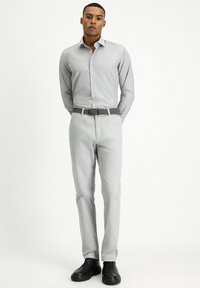 Grijze button-up shirt met fijne verticale strepen, gecombineerd met lichtgrijze broeken en zwarte instappers. Effen kleur riem met een gestructureerde afwerking.