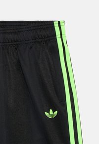 Czarne spodnie sportowe z neonowymi zielonymi paskami po bokach i logo Adidas. Posiadają teksturowane wykończenie i elastyczny pas.