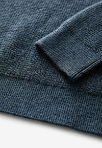 Tessuto a maglia blu scuro con una superficie texture, caratterizzato da polsini e orlo a coste. Il materiale sembra morbido e leggermente elasticizzato.