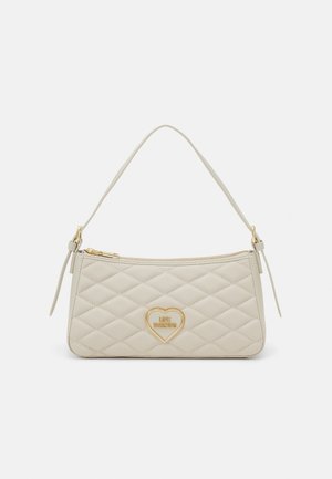 Beige gesteppte Handtasche mit einem einzelnen Riemen, goldfarbenem Reißverschluss und goldfarbenem herzförmigem Logoemblem in der Mitte.