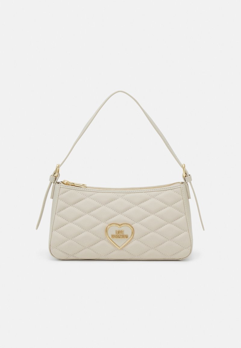 Sac à main matelassé beige avec une bandoulière unique, une fermeture éclair dorée et un logo en forme de cœur doré au centre.