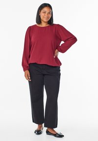 Bordowa bluzka na długi rękaw z bufkowymi rękawami, zestawiona z czarnymi spodniami o szerokich nogawkach i czarnymi balerinami. Gładka tkanina o subtelnej fakturze.