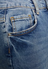 Ljusblå denimjeans med en synlig bakficka med synlig sömnad och en metallnubbdetalj. Mjuk textur med lätt blekning.