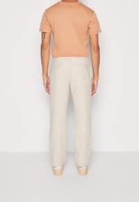 Beiga linnebyxor med rak passform, med två bakfickor och subtil textur. Matchas med en persikofärgad T-shirt, sedd från baksidan.