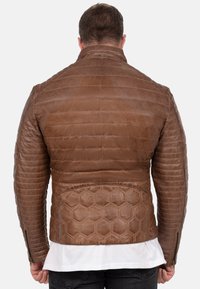 Bruine leren jas met quilted stiksel, hexagonale patronen accenten op de rug, en ritsmanchetten. Het heeft een rechtopstaande kraag.