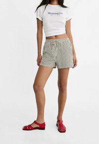 Biały krótki t-shirt z niebieskim napisem, zestawiony z czarno-białymi szortami w paski z troczkiem w pasie. Jasnoczerwone sandały z wycięciami.