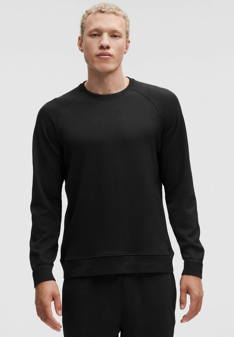 Sudadera negra de manga larga con un patrón texturizado, escote redondo y puños y dobladillo de canalé. Diseño ajustado, estilo minimalista.
