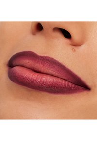 Matte mørk bær leppestift fremhever fyldige lepper, med en myk gradienteffekt og en teksturert finish mot jevn hud.