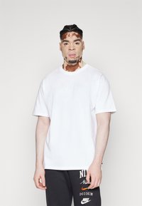 Tricou alb din bumbac, cu guler rotund și mâneci scurte, având un logo Nike subtil brodat pe piept.