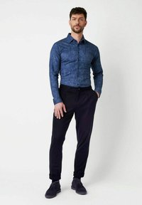 Blaues Button-Down-Hemd mit einem strukturierten Muster, kombiniert mit schwarzen schmal zulaufenden Hosen und dunkelgrauen Schuhen. Das Hemd hat einen Kentkragen.