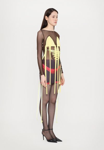 Schwarzmesh-Kleid mit gelben Akzenten, Spitzenrand und langen Bändern. Durchsichtiger Oberteil und enganliegender Rock, kombiniert mit schwarzen High-Heels.