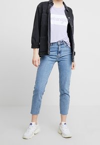 Černá džínová bunda přes světle fialové tričko s logem "Wrangler", doplněná světle modrými zkrácenými džíny a bílými teniskami.