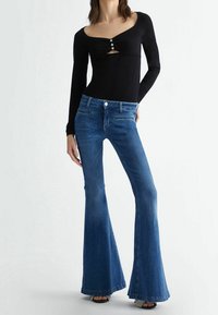 Body nero a maniche lunghe con scollo a V e tre bottoni decorativi sul petto, abbinato a jeans in denim blu a zampa d'elefante.