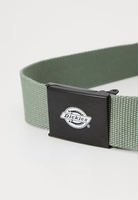 Zelený tkaný opasok s textúrovaným povrchom a čiernou kovovou sponou s obručou a textom "Dickies."