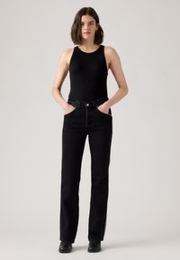 Zwarte geribbelde bodysuit gecombineerd met hoge taille zwarte jeans met zijstrepen, rechte pijpen en voorzakken.