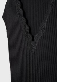 Detailný záber na čiernu rebrovanú látku s vlnitým čipkovým lemom pozdĺž V-tvarového výstrihu.