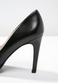 Escarpin en cuir verni noir avec un bout pointu et un talon aiguille effilé, présentant une finition lisse et brillante.