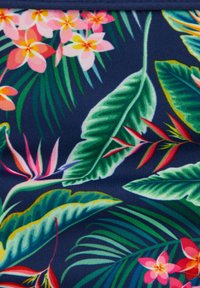 Tissu floral tropical avec de grandes feuilles vertes, des fleurs roses et orange, et des accents rouges sur un fond bleu foncé.