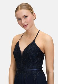 Robe bleu marine avec broderies florales, buste transparent et bretelles ajustables. Présente une taille cintrée et un design de jupe fluide.