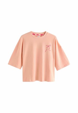Light pink, oversized cotton T-shirt with short sleeves. Features a small, pink bow design on the chest. Simple and casual design.