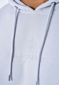 Felpa leggera blu con cappuccio e cordoncino, caratterizzata da un logo ricamato e dalla scritta "PROJECT X PARIS" sul petto in filo bianco.