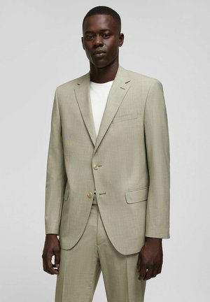 Hellgrüner Blazer aus strukturiertem Stoff mit Reverskragen, zwei Knöpfen und einer Brusttasche, kombiniert mit einem weißen Hemd.