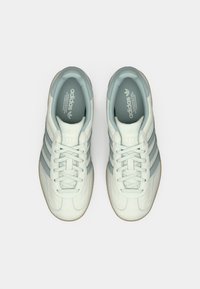 Ανοιχτό μπλε αθλητικά παπούτσια Adidas με λεία επάνω επιφάνεια, τρεις πιο σκούρες μπλε ρίγες και ταμπά λαστιχένια σόλα, με στρογγυλεμένη μύτη και κλείσιμο με κορδόνια.