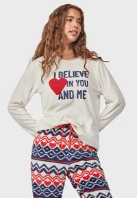 White sweatshirt with "I BELIEVE IN YOU AND ME" text, featuring a red heart accent. Paired with blue patterned pajama pants with red hearts.
