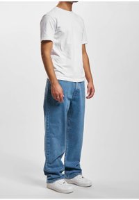 Camiseta blanca de algodón con cuello redondo combinada con pantalones vaqueros de denim azul de corte holgado. Zapatillas deportivas blancas completan el conjunto.
