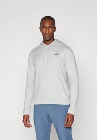 Hoodie cinza claro em um tecido macio com um bolso frontal e um logotipo preto no peito. Possui capuz com cordão e punhos ajustados.