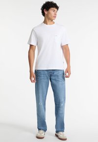 Valge lühikeste袖tega t-särk rinnataskuga, koos helesiniste jeanšortidega, millel on kerge kahjustus, ja beežide spordijalatsitega.