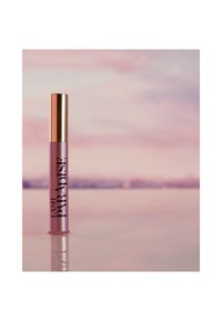 Mascara Lash Paradise dans un tube rose givré avec un capuchon métallique doré, arborant un texte noir en gras indiquant "LASH PARADISE." Surface réfléchissante.