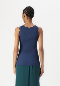 Marineblauw geribbelde mouwloze top met geschulpte kanten rand langs de halslijn. Getailleerde pasvorm, gemaakt van rekbare stof.