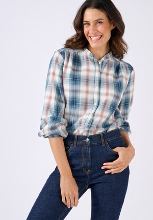 Chemise à carreaux avec col, en blanc, bleu et rouge, avec fermeture à boutons et manches retroussées, associée à un jean taille haute bleu foncé.