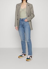 Šedý kostkovaný blazer přes světle zelený přiléhavý top, kombinovaný s riflemi vysokého pasu v světle modré barvě a barevnými teniskami s bílými akcenty.