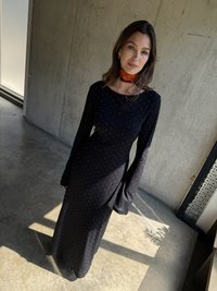 Robe noire à manches longues avec un corsage ajusté et des manches évasées, ornée de pois blancs. Le tissu a une texture douce.