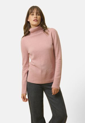 Jasnoróżowy sweter z golfem wykonany z miękkiego materiału, z prążkowanymi mankietami i dolnym wykończeniem, w zestawieniu z ciemnymi spodniami typu wide-leg.